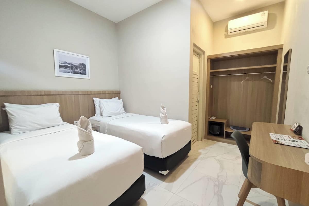 Une chambre d’hôtel avec deux lits, une armoire en bois, une petite table et un tableau encadré au mur.