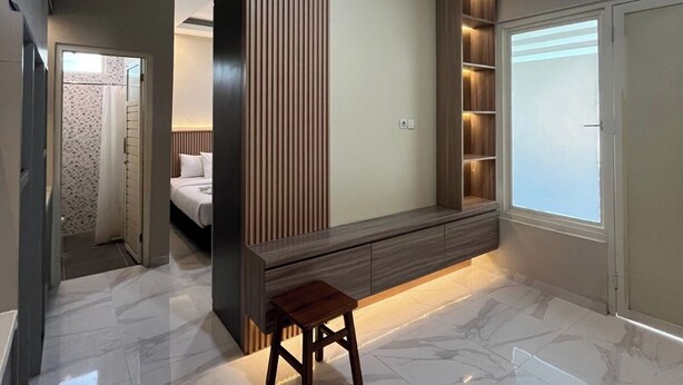 A modern bedroom with a built-in wardrobe, a bedside table, and a window with blinds. - El Nipa Hotel Labuan Bajo (Labuan Bajo)
