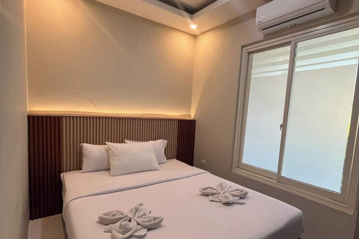 Une chambre d’hôtel moderne dotée d’un grand lit, d’une tête de lit intégrée, d’un appareil de climatisation et d’une fenêtre avec stores.