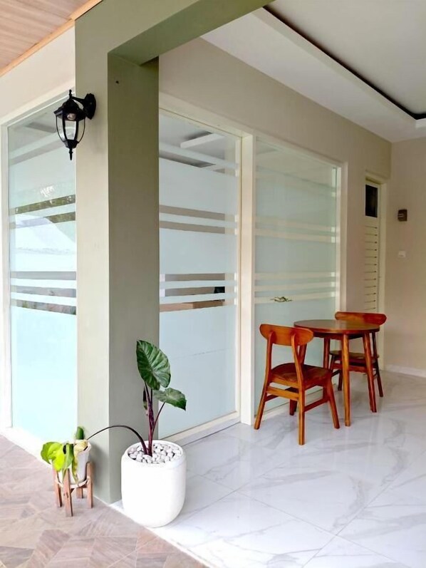 A modern interior with a glass door, a small table with chairs, and a potted plant. - El Nipa Hotel Labuan Bajo (Labuan Bajo)