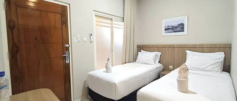 A hotel room with two single beds, a wooden door, a small table with a menu, and a framed picture on the wall.