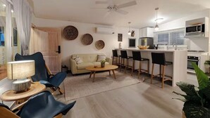 Ein modernes Wohnzimmer mit Sofa, Sesseln, einem Couchtisch und einer Küchenzeile mit Mikrowelle und Herd.