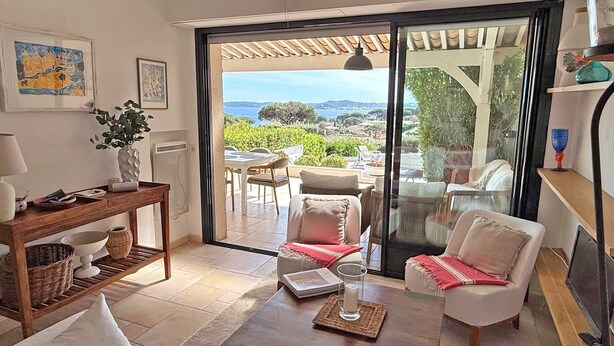 Sala de estar com vista para o mar, área de refeições e porta de vidro deslizante para o exterior.