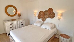 Quarto com cama, cômoda, espelho redondo, luminárias fixadas na parede e um objeto decorativo na parede.