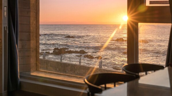 Une vue sur l’océan, prise à travers une fenêtre ornée d’une rambarde, avec une chaise et une table.