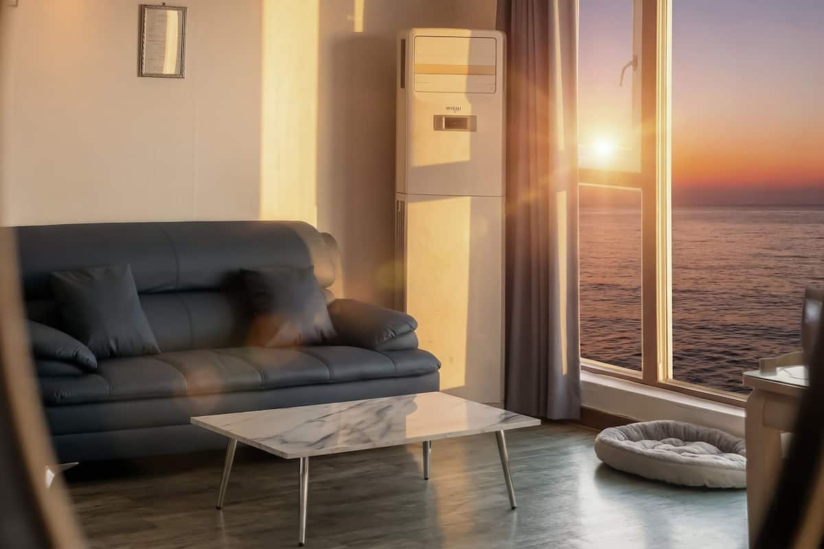 A modern living room with a sofa, a small table, and a view of the sea at sunset.