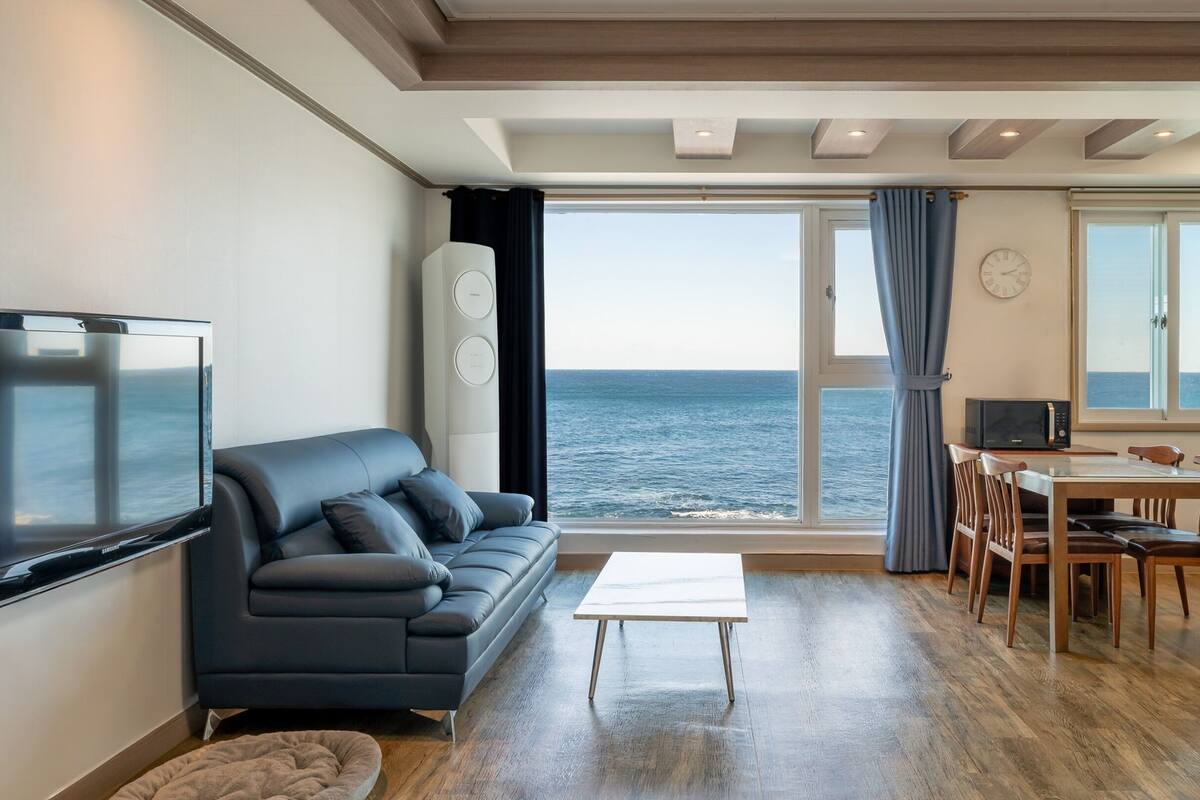 A modern living room with a sofa, TV, and a view of the sea.