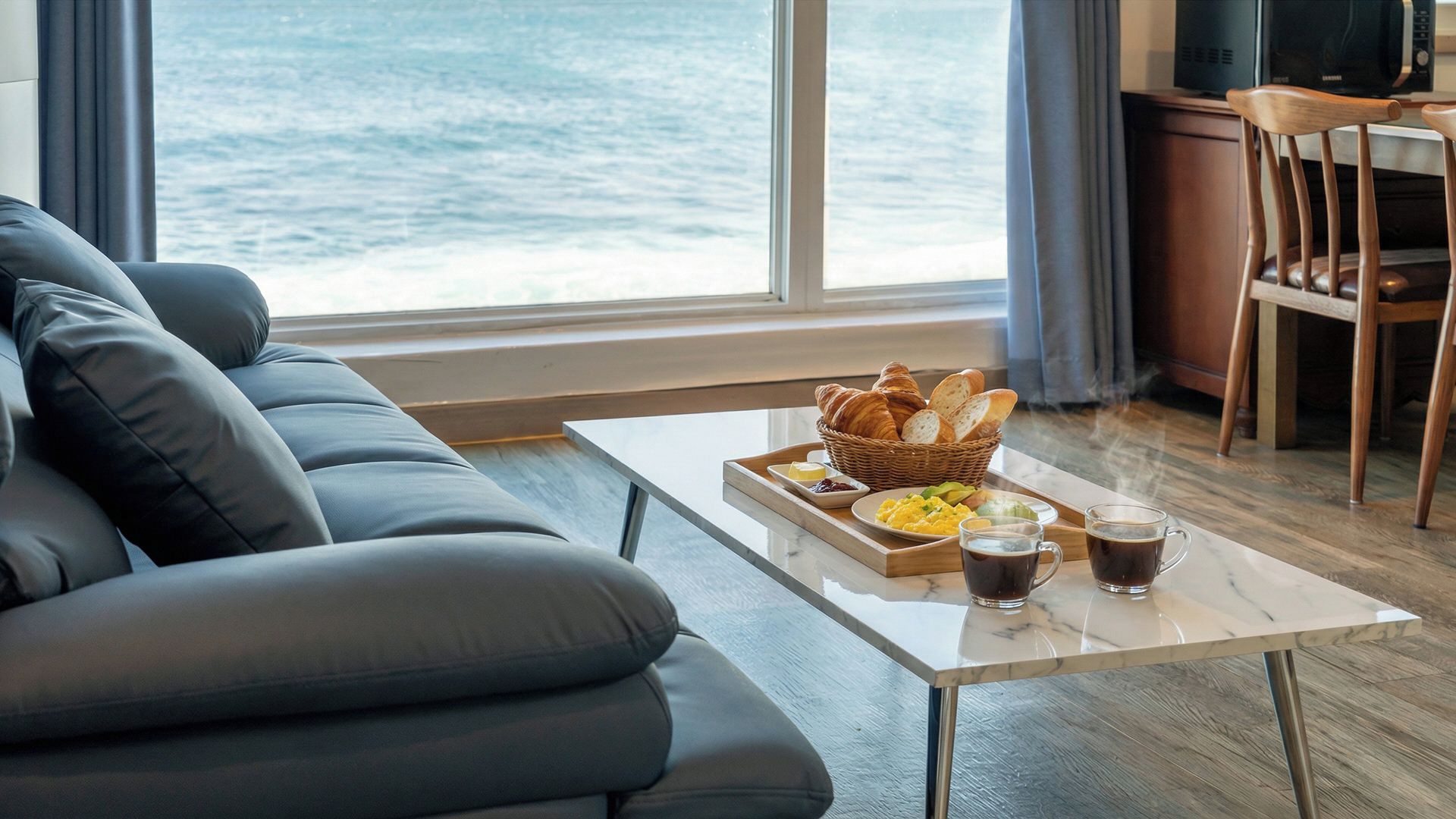 Una sala de estar moderna con un sofá de cuero, una bandeja de desayuno con croissants y huevos revueltos, y una mesa de centro con dos tazas de café.