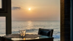 A table with a glass and a chair, facing a view of the ocean with the sun setting in the background. - Haru Stay Donghae (Donghae)