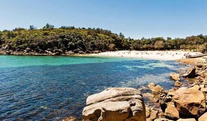 A beach with clear turquoise water, rocky shoreline, and a sandy beach with people.