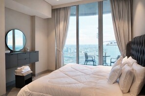 Ein modernes Hotelzimmer mit einem großen Bett, einem Schminktisch mit Spiegel und Blick auf eine Stadtlandschaft durch raumhohe Fenster.