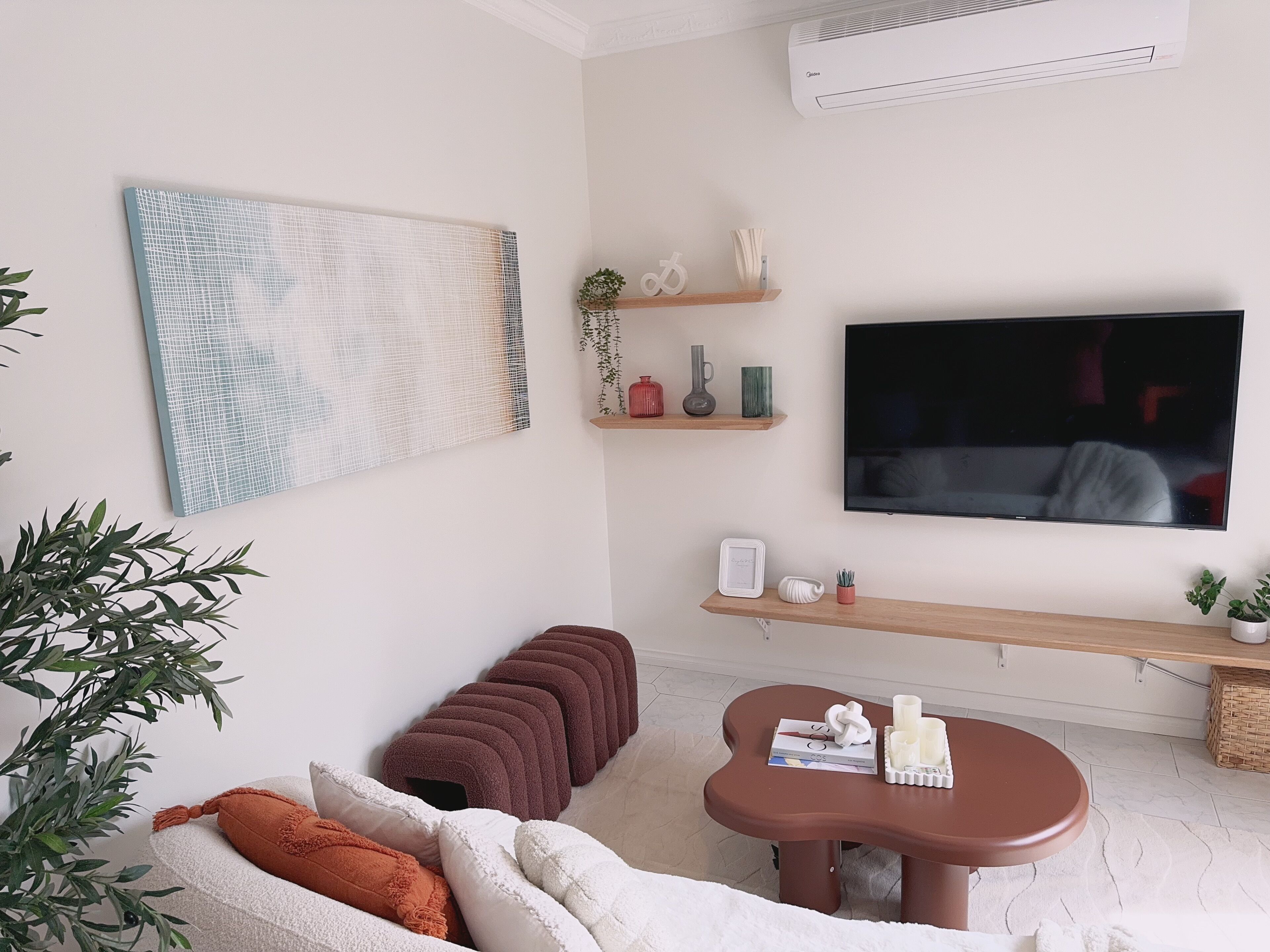 Een moderne woonkamer met een grote televisie, een bank, een salontafel en decoratieve objecten op planken.