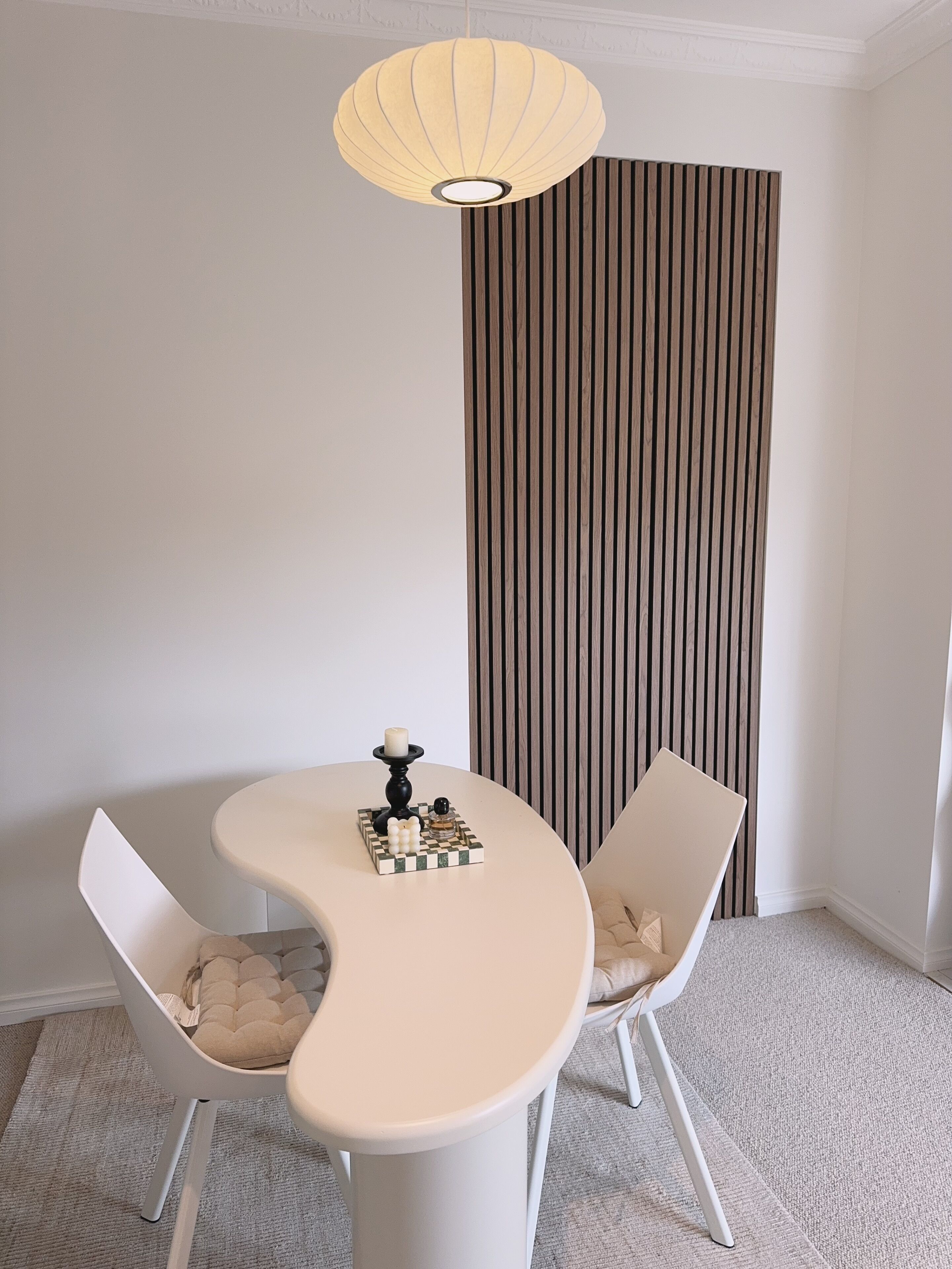 A modern dining area with a round table, two white chairs, a decorative candle centerpiece, and a striped wall.