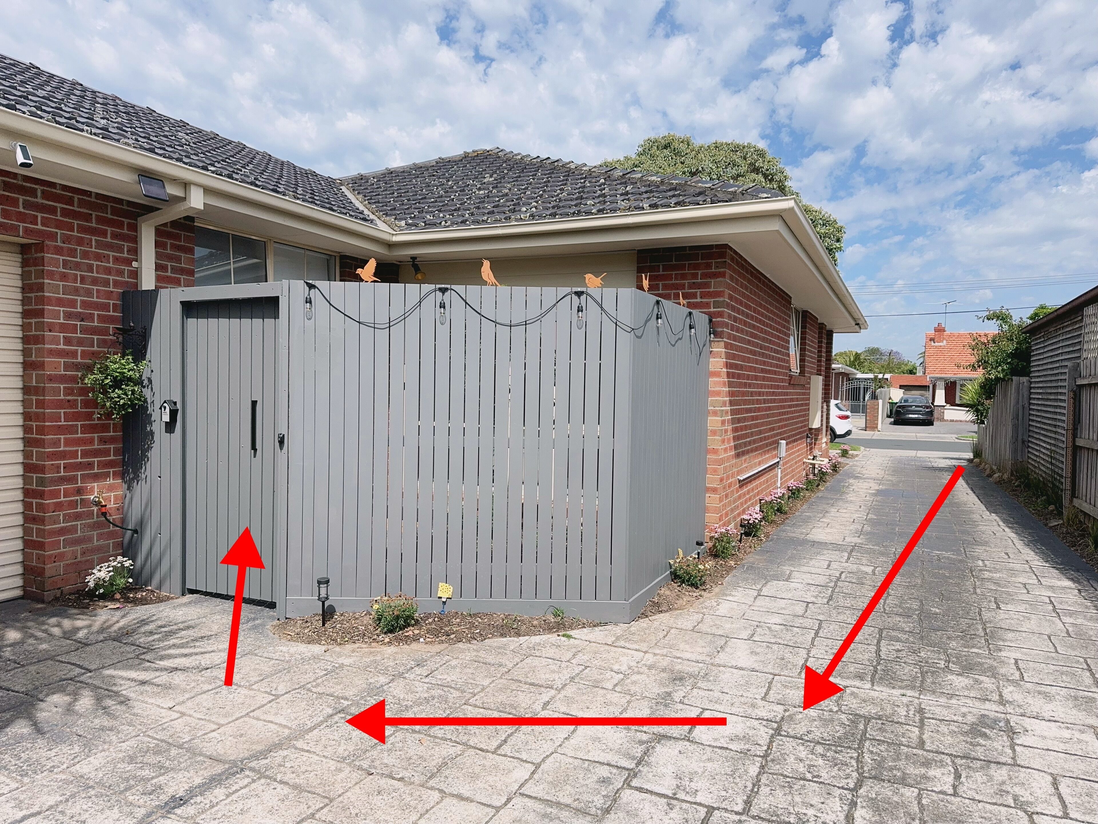 Een woonhuis met een grijze metalen poort, bakstenen muren en een verharde oprit.