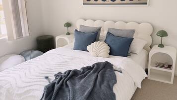 Een net opgemaakt bed met een wit- en blauw geborreld beddekleed, een blauwe gebreide plaid en een wandairconditioner.