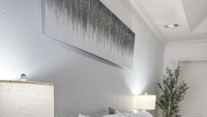 Ein ordentlich bezogenes Bett mit weißer Bettwäsche, ein Nachttisch mit einer Lampe und ein Wandbild.