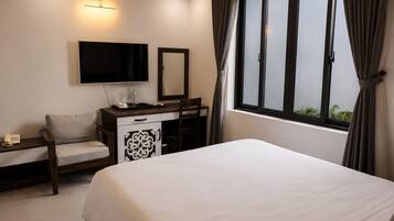 Habitación de hotel con cama, escritorio con televisor de pantalla plana, silla, mesita de noche con lámpara y ventana con cortinas.