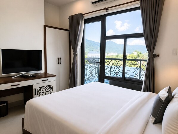 A hotel room with a bed, a desk with a TV, and a balcony with a view of mountains. - Nam Hai Hotel Con Dao (Ho Chi Minh City)