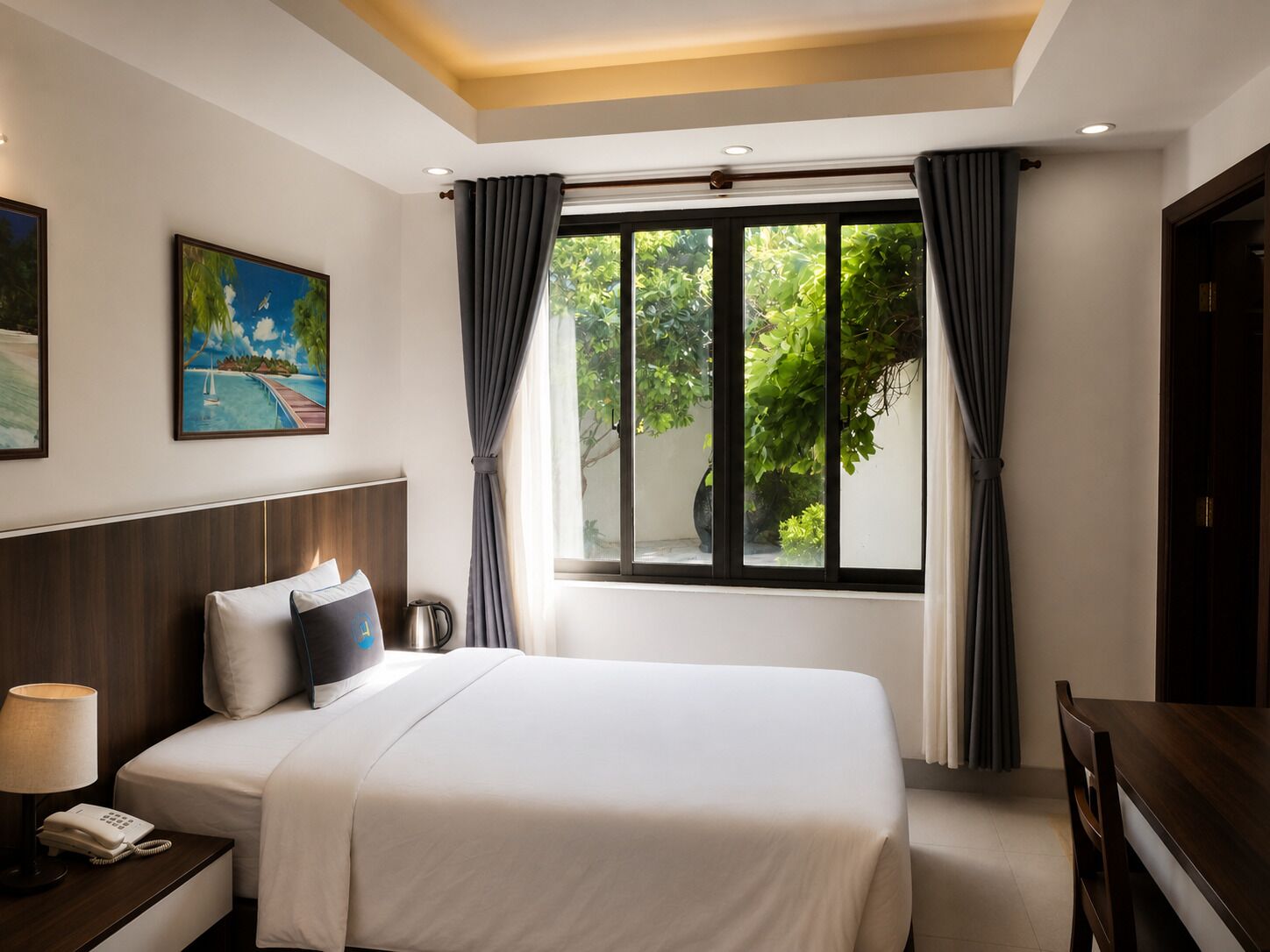 A hotel room with a bed, bedside table with a lamp and phone, a painting on the wall, and a window with curtains.
