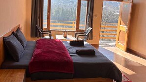 A bedroom with a bed, a wooden bench, a view of a mountain, and a door with a number. - Mountain View -bedroom,  bed & breakfast in welcoming Manali (Manali)