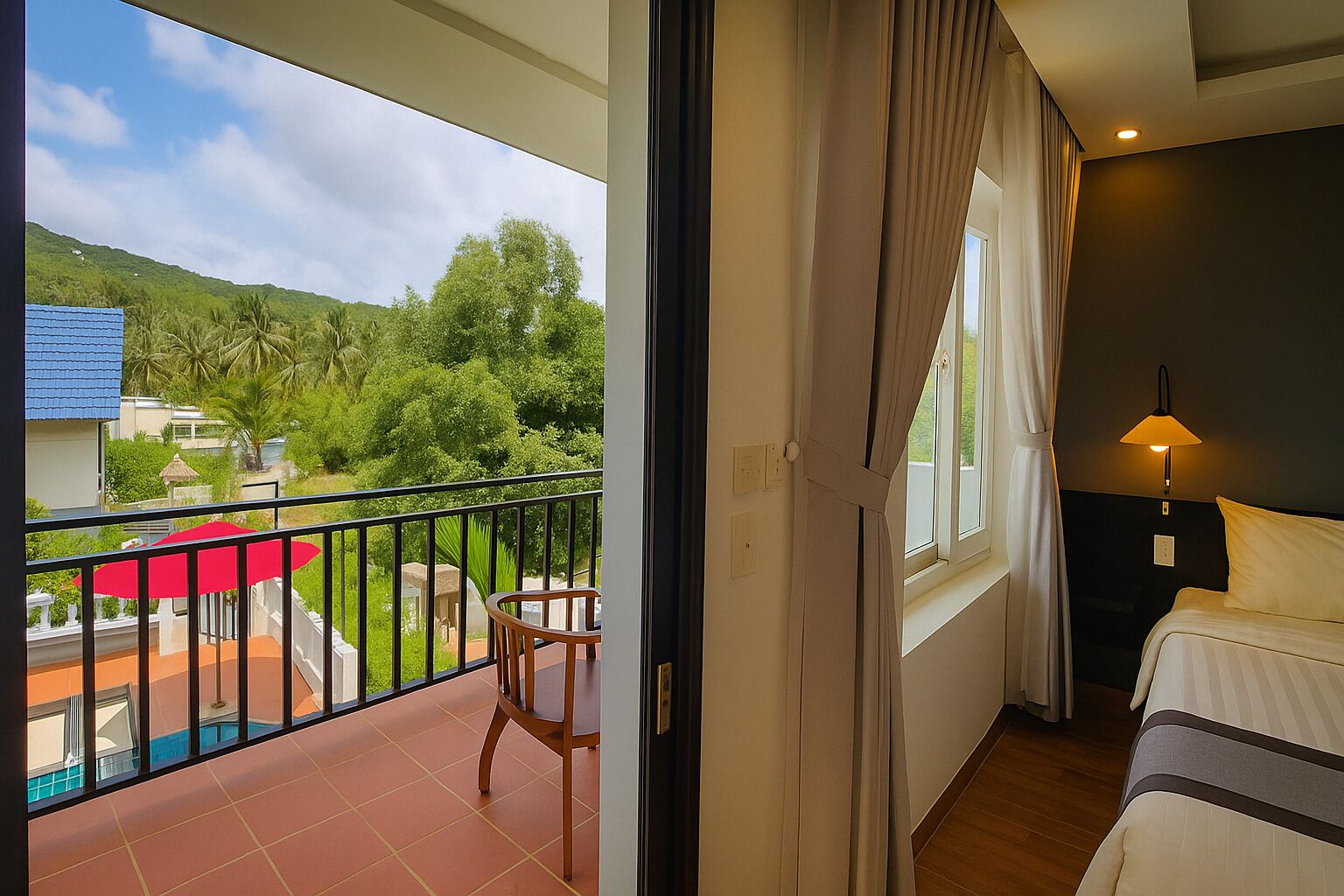 A hotel room with a balcony, a bed, a nightstand, a lamp, and a view of greenery and buildings outside.