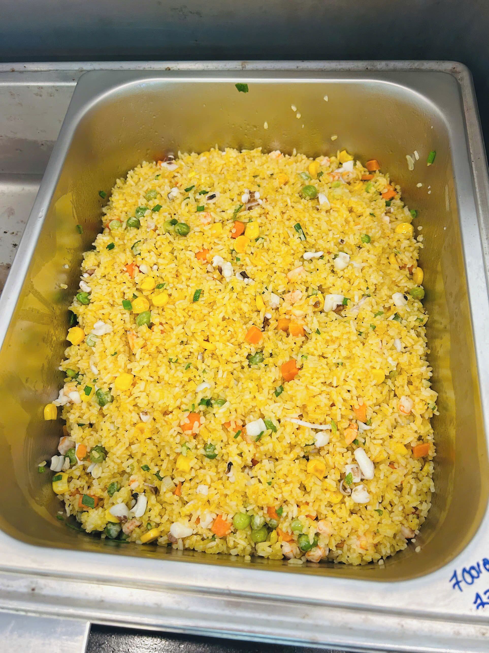A large metal tray filled with yellow fried rice mixed with vegetables and eggs.