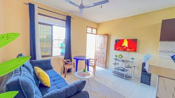A living room with a sofa, a TV mounted on the wall, a ceiling fan, and a small table with chairs.