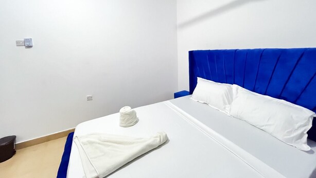 A hotel room with a single bed, a ceiling fan, and a blue headboard. - Sunset Suites Mtwapa (Mtwapa)