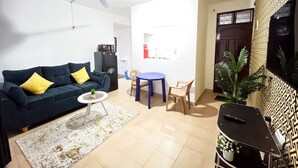 A living room with a sofa, a coffee table, a dining table with chairs, a ceiling fan, and a TV on a stand. - Sunset Suites Mtwapa (Mtwapa)