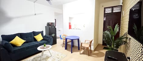 A living room with a sofa, a coffee table, a dining table with chairs, a ceiling fan, and a TV on a stand.