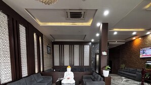 Un vestíbulo con una estatua de Buda, sofás grises, piso de mármol y una pantalla de televisión.