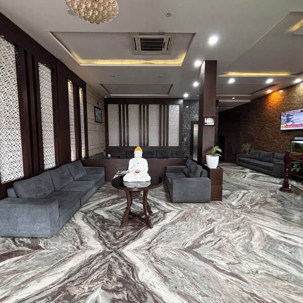 A lobby with a Buddha statue, grey sofas, a marble floor, and a TV screen.