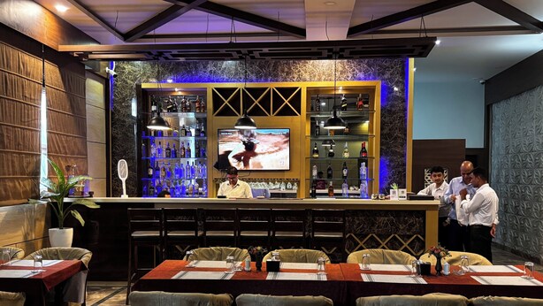 Un restaurante con barra, varias mesas con sillas y una pantalla de televisión.