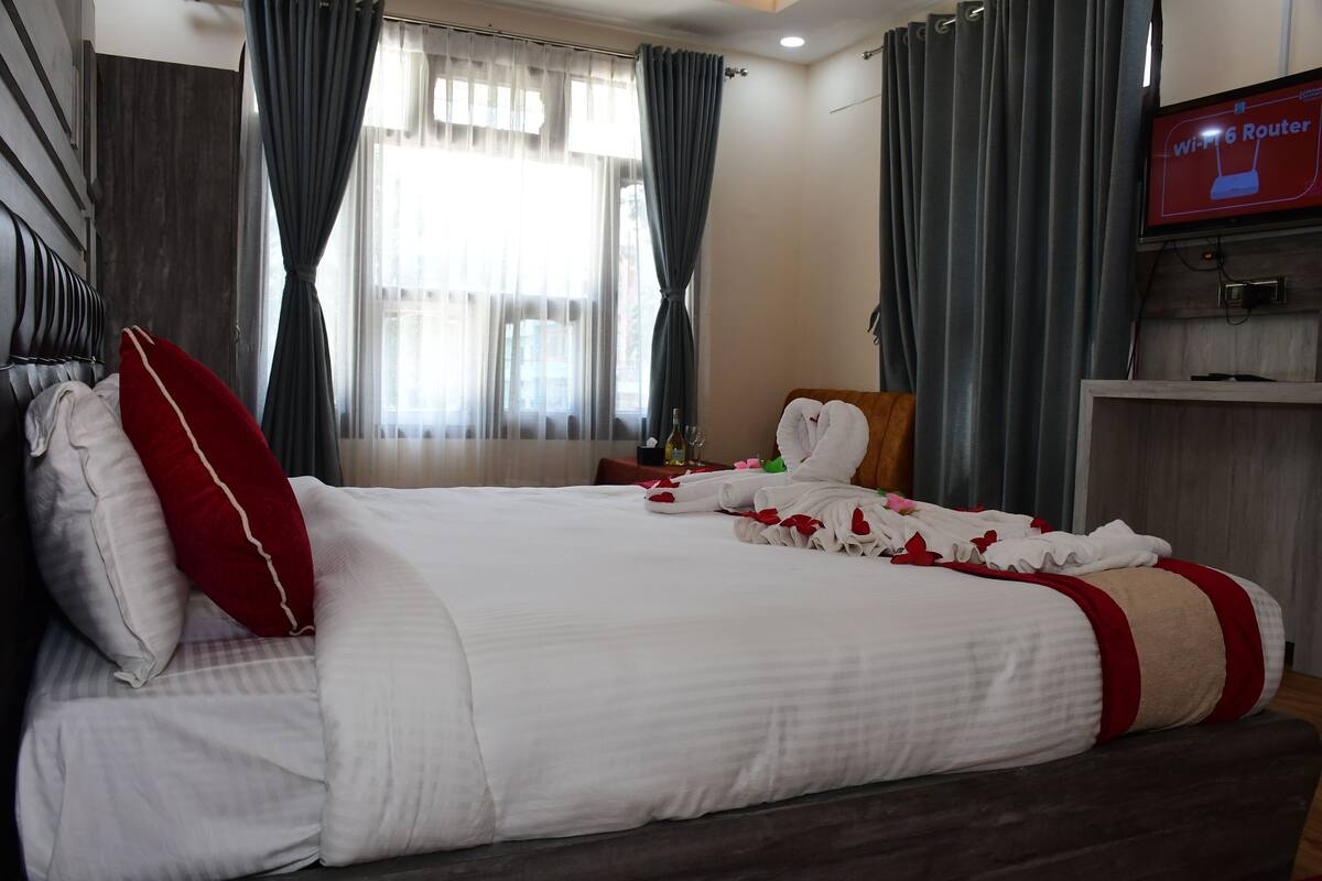 A hotel room with a large bed, a TV on the wall, and a window with curtains.