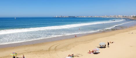 A beach with people sunbathing, umbrellas, and a distant city skyline.