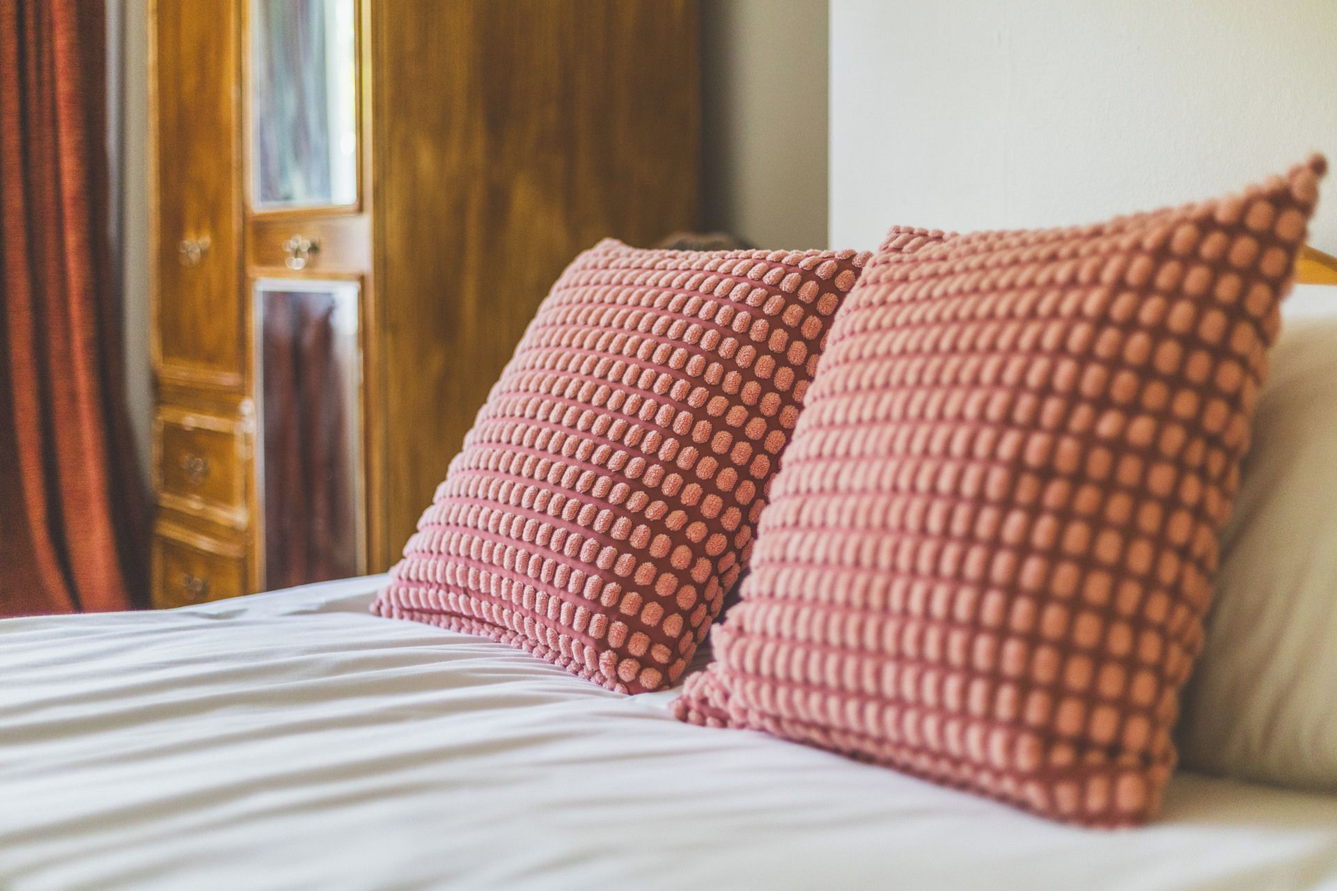 A bed with white bedding and two pink pillows with a textured pattern.