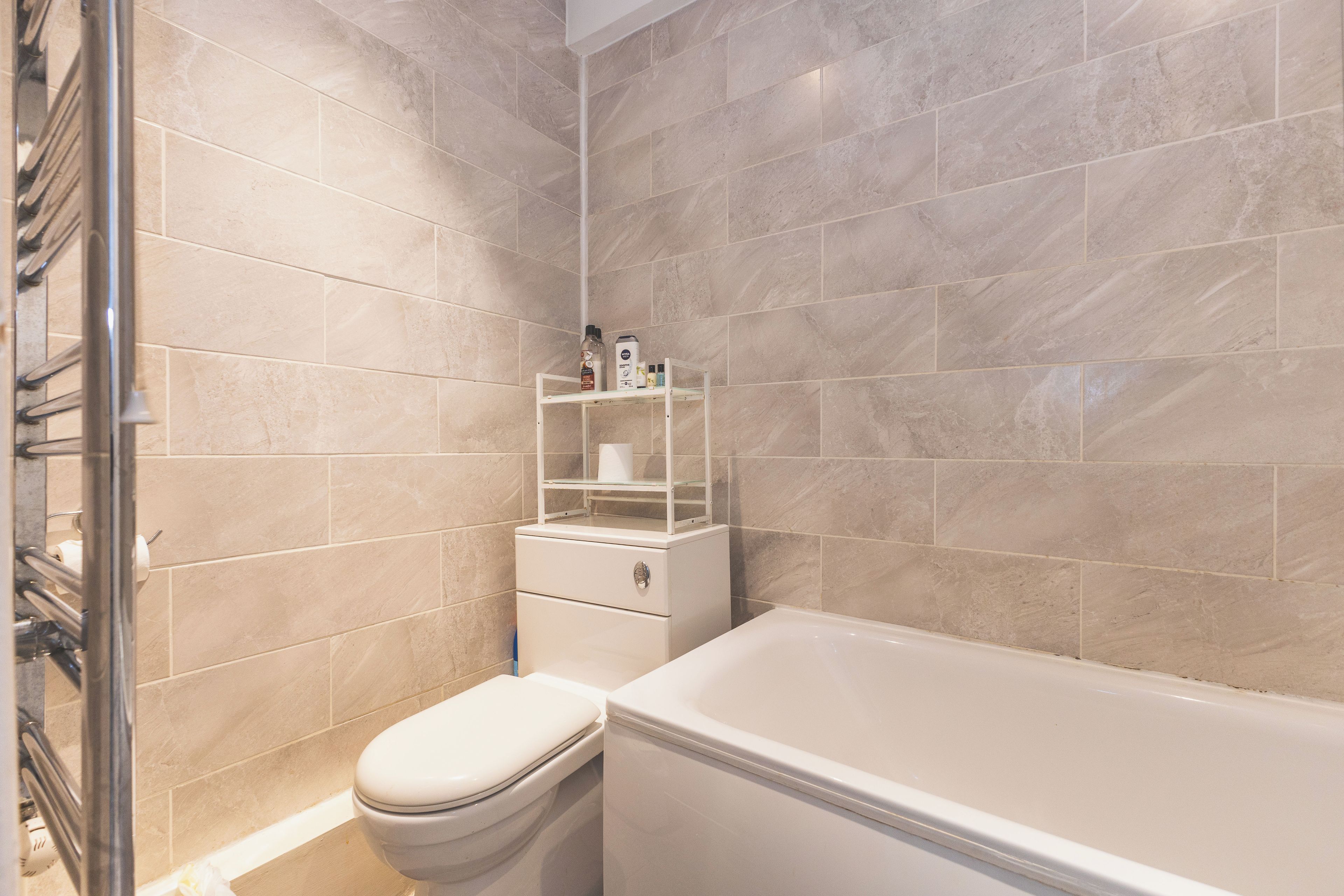 A bathroom with a bathtub, toilet, and a shelf with toiletries.