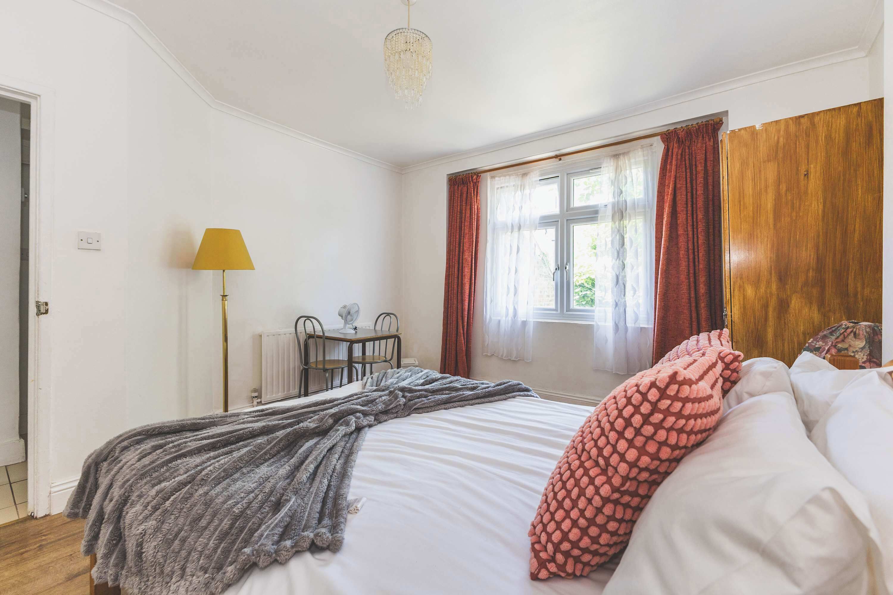 A bedroom with a bed, a bedside table, a lamp, a window with curtains, and a radiator.