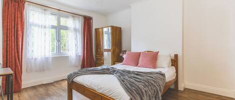 A bedroom with a wooden bed, a wardrobe, a desk, and a window with curtains.