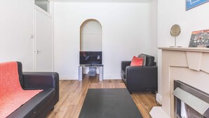 Ein Wohnzimmer mit Fernseher, zwei Sofas, einem Kamin und Holzboden.