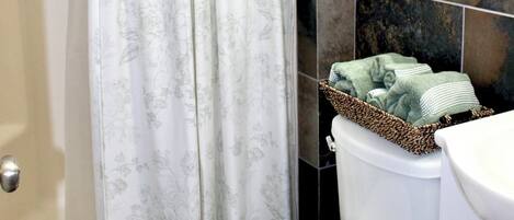 A bathroom with a shower curtain, a toilet, a sink, and a shelf with plants.