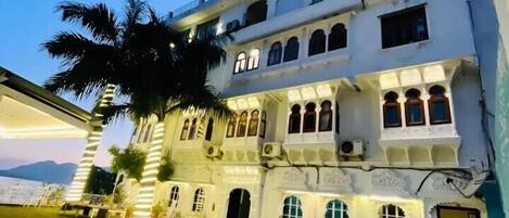 A multi-story building with a courtyard, arched windows, and a view of the sea.