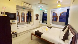 Habitación de hotel con cama, televisor, ventilador de techo y ventanas con marcos decorativos.