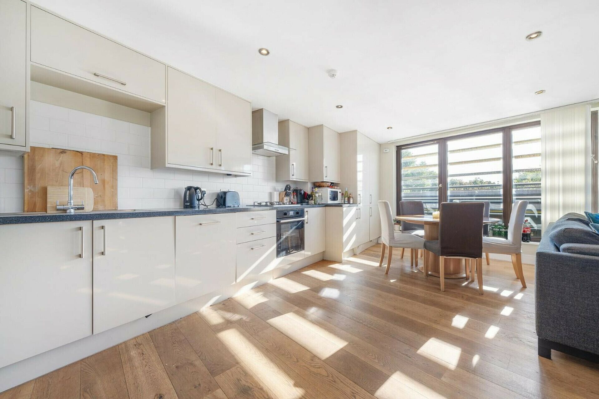 A modern kitchen with white cabinets, a wooden countertop, and a dining area with a table and chairs.