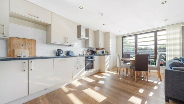 Une cuisine moderne avec des meubles blancs, un plan de travail en bois et un coin repas comprenant une table et des chaises.