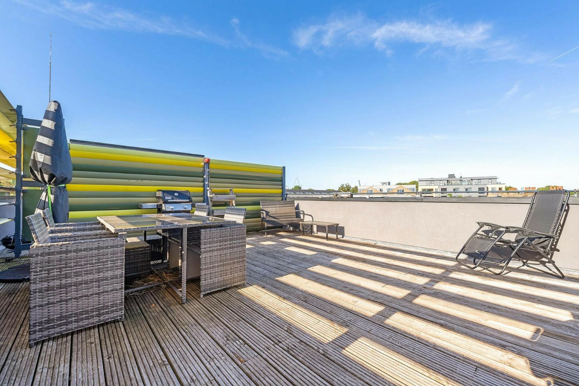 A rooftop deck with outdoor furniture, a grill, and a view of the cityscape.