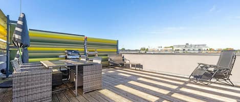 A rooftop deck with outdoor furniture, a grill, and a view of the cityscape.
