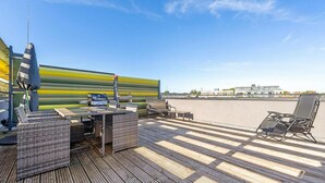 Une terrasse sur le toit, aménagée avec du mobilier d’extérieur, un barbecue et offrant une vue sur le paysage urbain.