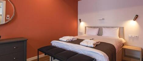 Un dormitorio con cama, mesitas de noche, un banco, cómoda y espejo.
