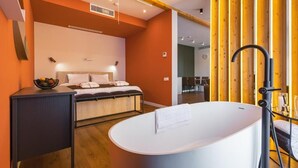 Ein modernes Schlafzimmer mit einem großen Bett, einem Nachttisch mit Fruchtschale, einer weißen Badewanne und Holzpaneelen an der Wand.